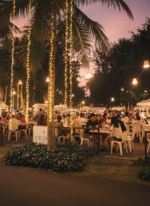 Visitors dining beneath illuminated palm trees at Cicada Market in Hua Hin during the evening.