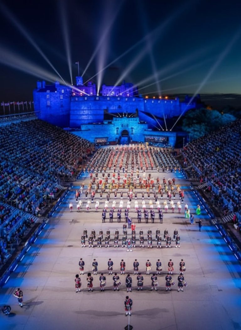 Performers marching in formation during the Royal Edinburgh Military Tattoo beneath the illuminated Edinburgh Castle.