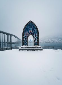 The Gateway to the Arctic monument standing beside Tromsø Bridge on a snowy winter day.