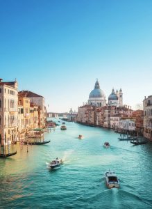 Boats traveling along Venice's Grand Canal with the Basilica di Santa Maria della Salute in the distance.