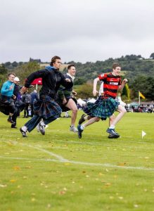 Competitors race across the field wearing kilts during a Scottish Highland Games event.