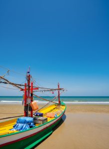 Traditional fishing boat resting on the sandy beach of Hua Hin beneath a clear blue sky.