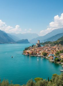 Panoramic view of Limone sul Garda on the shores of Lake Garda with colorful waterfront buildings, a medieval castle tower, and mountains surrounding the lake.