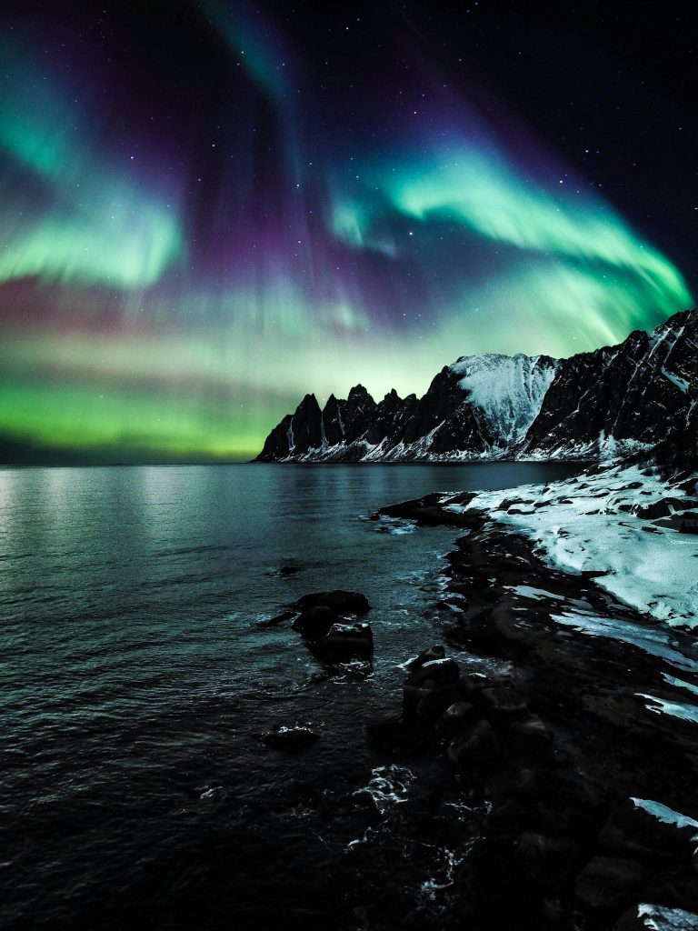 Northern Lights dancing above snowy mountains and Arctic waters in Norway
