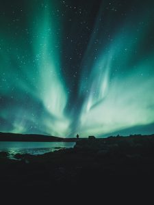 Northern Lights dancing above an Arctic lake in Norway beneath a star filled winter sky.