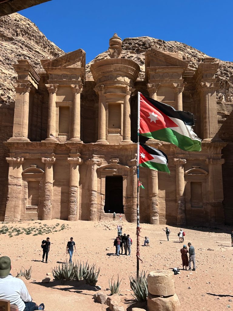 The iconic Treasury at Petra with Jordanian flags flying in front of the ancient sandstone monument.