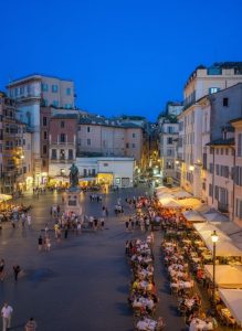 Evening view across Piazza del Popolo with outdoor restaurants, historic buildings, and visitors enjoying the square in Rome.