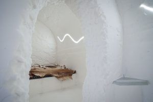 Family room inside the Sorrisniva Ice Hotel in Alta, Norway, featuring hand carved snow walls, ice architecture and reindeer hide covered beds.