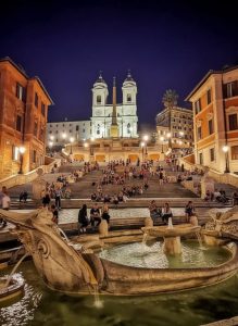 The Spanish Steps and Trinità dei Monti church illuminated at night with visitors relaxing on the famous staircase.