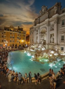 The illuminated Trevi Fountain in Rome surrounded by visitors enjoying the landmark after sunset.