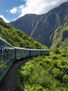 Scenic blue train travelling through the lush mountains of Peru's Sacred Valley on the route to Machu Picchu.